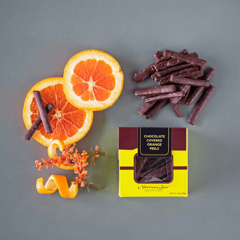 Dark chocolate covered orange sticks on grey background with orange slices.