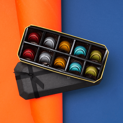 10 Piece BLACK Dark Chocolate Gift Box, opened to show two of each flavor dark chocolate and its colors and designs on an orange and blue background. Flavors: Jiquilisco Bay (97%), Maracaibo (88%), Tanzanie (75%), Pico Bonito (70%), Nyangbo (68%).