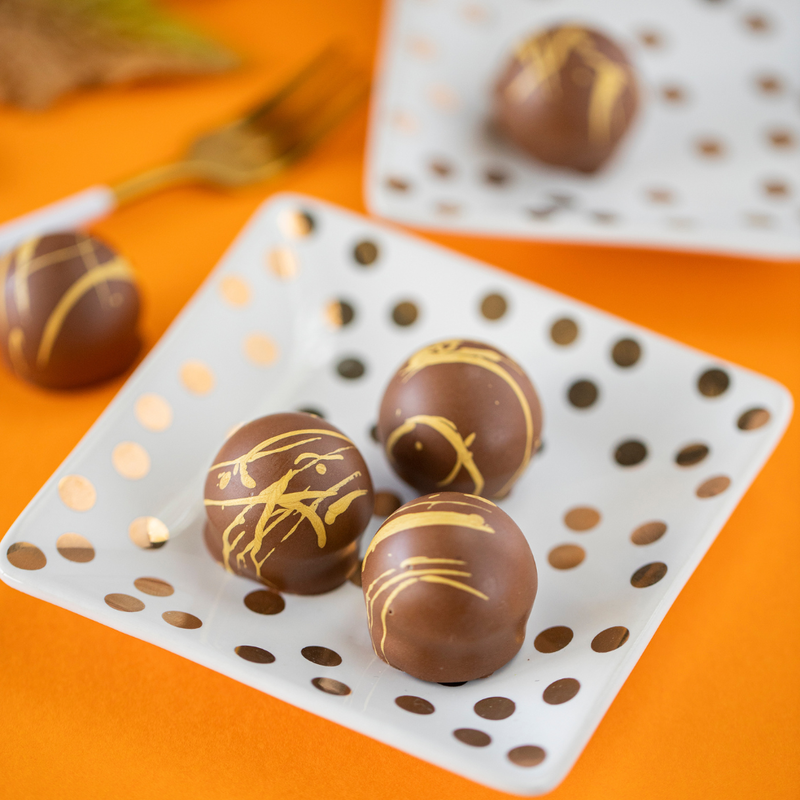 5 hazelnut praline truffles, sitting atop white plates with gold polka dots on an orange background. The truffles are arranged to showcase their circular shape and yellow and brown coloration.