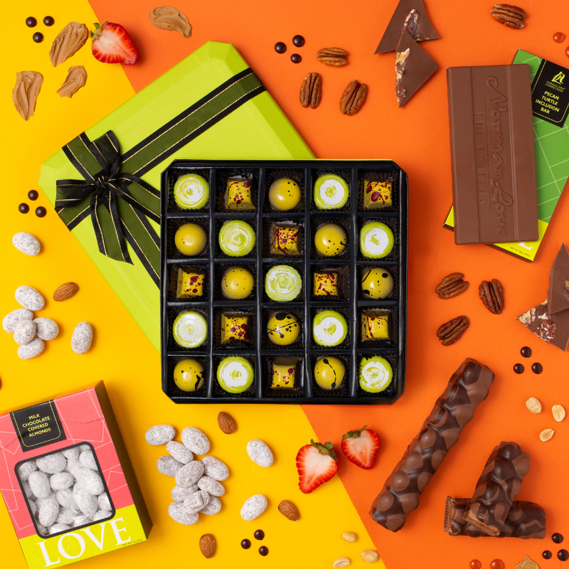 25 piece box of yellow and green colored chocolates, pink box of covered almonds (left); rectangle chocolate bar on green package; two chocolate bars (right) on yellow & orange background. Strawberries, almonds, pecans, peanuts & chocolate pieces.