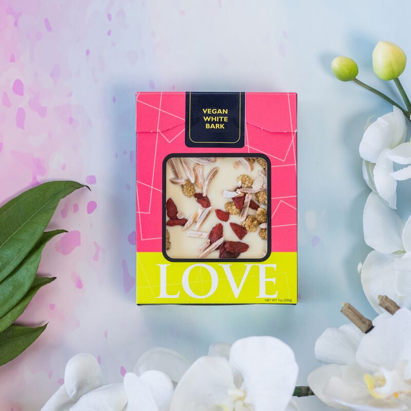 Vegan white chocolate bar in pink box on pink and blue background. 