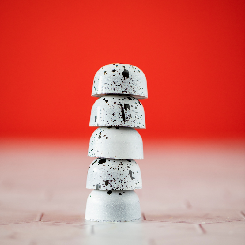 5 Cookies and Cream chocolates stacked one on top of another to form a column that showcases the mottled white and black design and the curved shape of the bonbons.