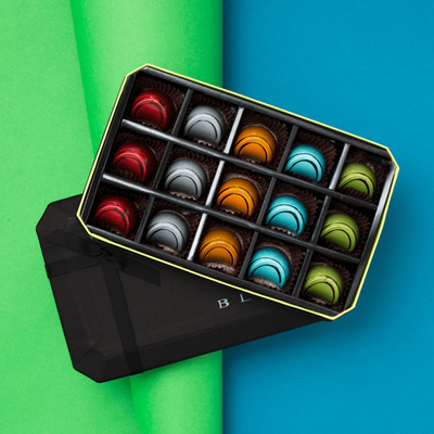 15 Piece BLACK Dark Chocolate Gift Box, opened to show three of each flavor dark chocolate and its colors and designs on a green and blue background. Flavors: Jiquilisco Bay (97%), Maracaibo (88%), Tanzanie (75%), Pico Bonito (70%), Nyangbo (68%).