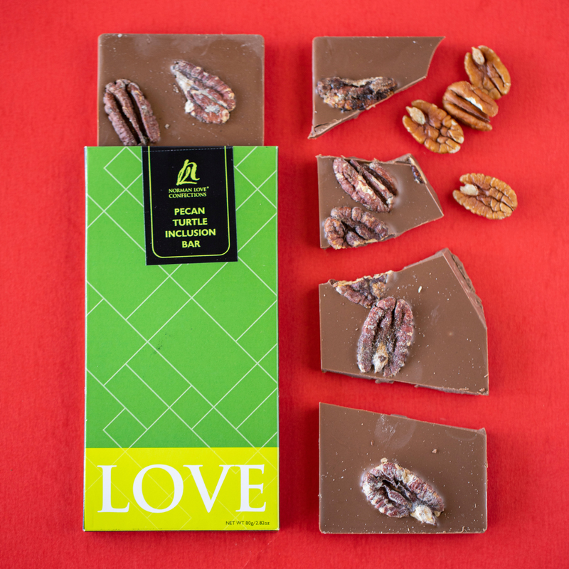 Green packaged pecan turtle chocolate bar with bar coming out of top and broken pieces to right on red background. Pecans scattered to right.