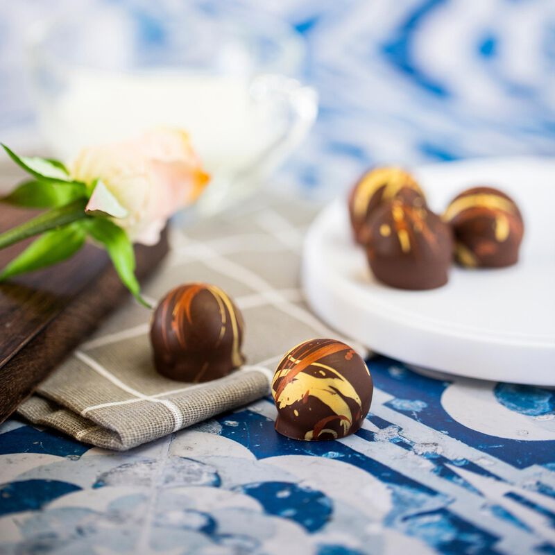 Five double shot espresso truffles, spread across a background featuring a napkin, rose, and white plate. The truffles are arranged to show their circle shape and yellow, orange, and brown coloration.