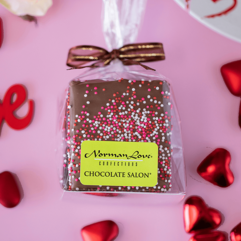 Chocolate covered graham crackers on pink background with red hearts. 