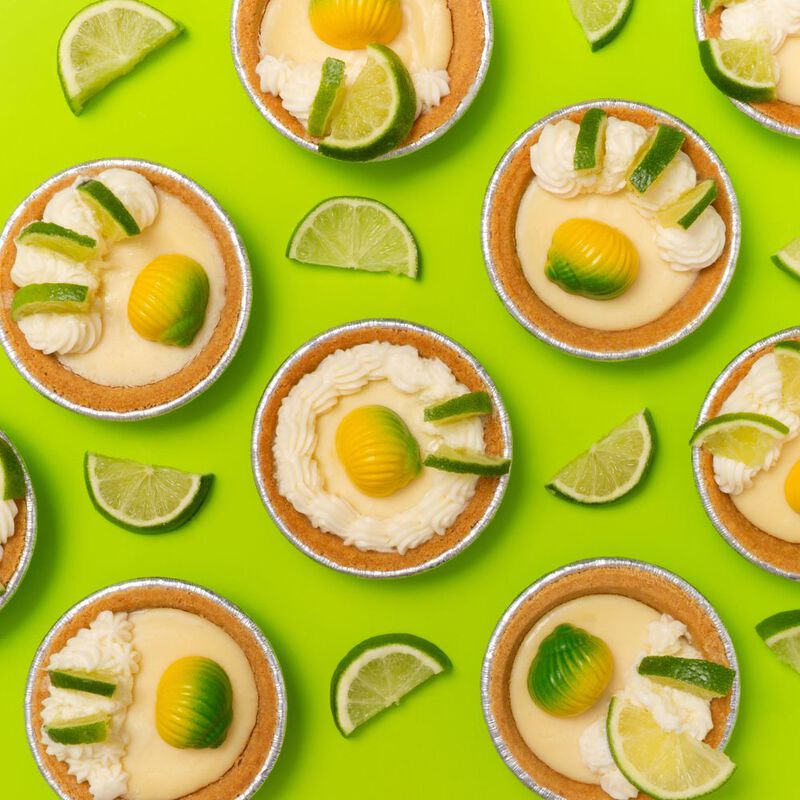 Key Lime Pie seashell-shaped chocolates on top of miniature key lime pies on a bright green background with lime wedges throughout