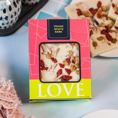 Vegan white chocolate bar in pink box on blue background.