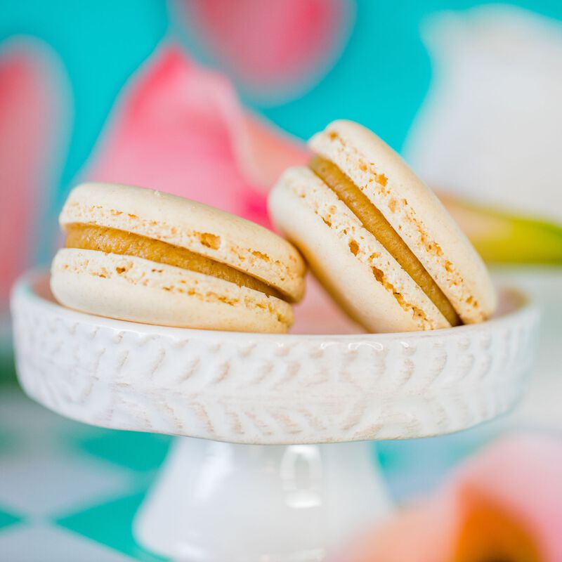 Two Vanilla French macarons displayed on a white dessert stand to show the ruffled edge of the cookie with a delightful gooey center. 