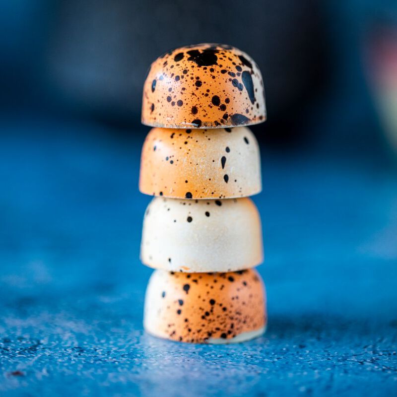Four Passionfruit Panna Cotta chocolates stacked on top of each other, showcasing each chocolate's orange and white coloration and black speckling