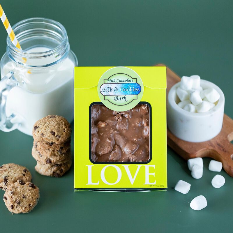 A package of milk and cookies bark with window packaging to show the product's texture, with a glass of milk, mini cookies, and marshmallows scattered around to evoke the product's components