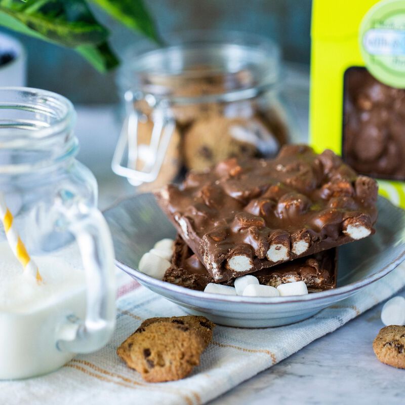A plate of milk and cookies bark, cut in pieces to show the marshmallow and cookie interior, with the packaged product nestled in the background
