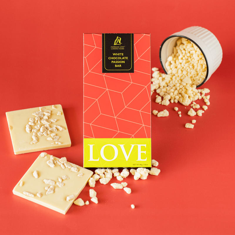 Two square pieces of white chocolate passion bar (left); rectangle bar in red packaging (center) with white chocolate in front; white chocolate falling out of tipped white bowl with black rim (upper right) on red background. 