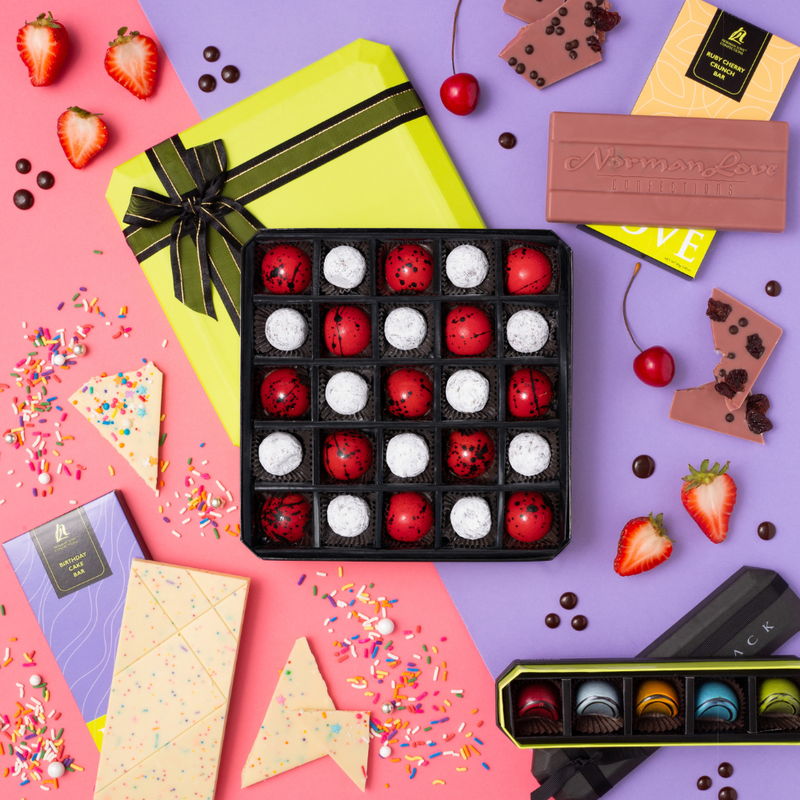 25 piece gift box of red & white bonbons; lime green lid with brown bow; rectangle white chocolate bar on purple package; pink colored chocolate bar; 5 piece multi-colored bonbons on black lid; pink & purple background with strawberries & sprinkles.