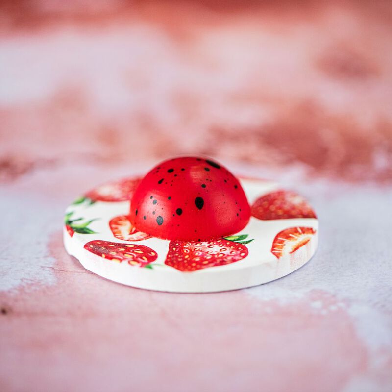 One Strawberry chocolate atop a coaster featuring images of strawberries on a textured pink background