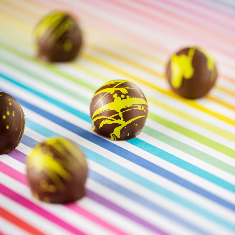 5 dark chocolate cream truffles on a rainbow-patterned background, focused to show the green cocoa butter design on each chocolate's shell