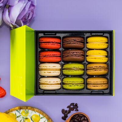 An open gift box displays twelve brightly colored French macarons in six delicious flavors: Lemon, Pistachio, Dark Chocolate, Raspberry, Caramel, and Vanilla. The gift box is on a purple background with flowers, raspberries, lemons and coffee beans.