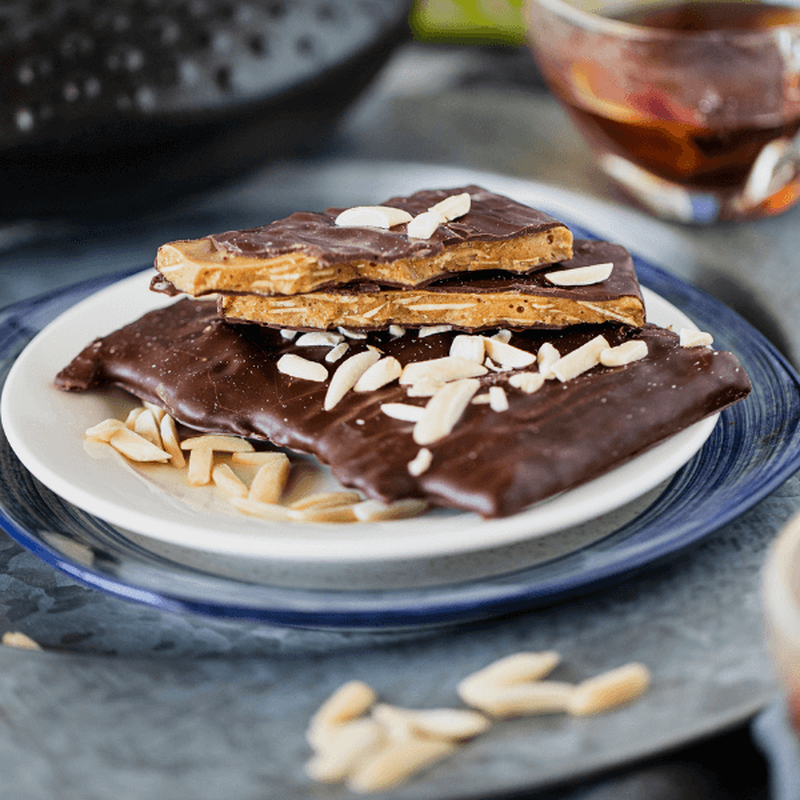 Chocolate covered toffee with almonds on white plate. 