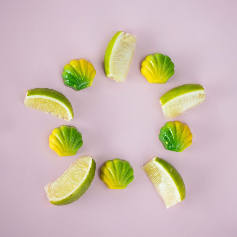 Green and yellow seashell truffles and lime slices displayed in a circle on a light pink backgroun