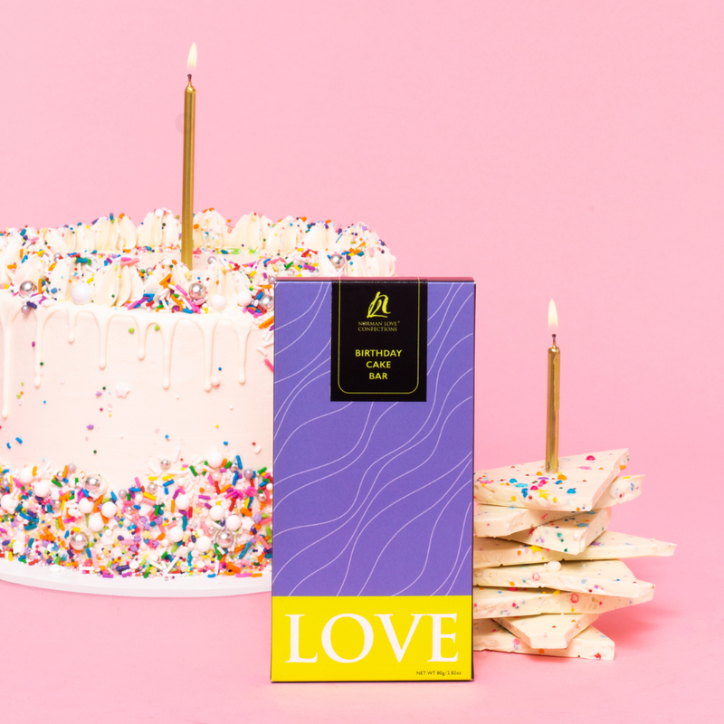 Purple packaged birthday cake chocolate bar on pink background. White frosted cake with sprinkles and gold candle(left); broken pieces of birthday cake bar with gold candle(right). 