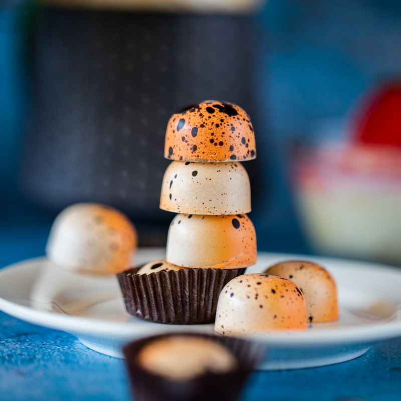 Four Passionfruit Panna Cotta chocolates stacked on top of each other, showcasing each chocolate's orange and white coloration and black speckling