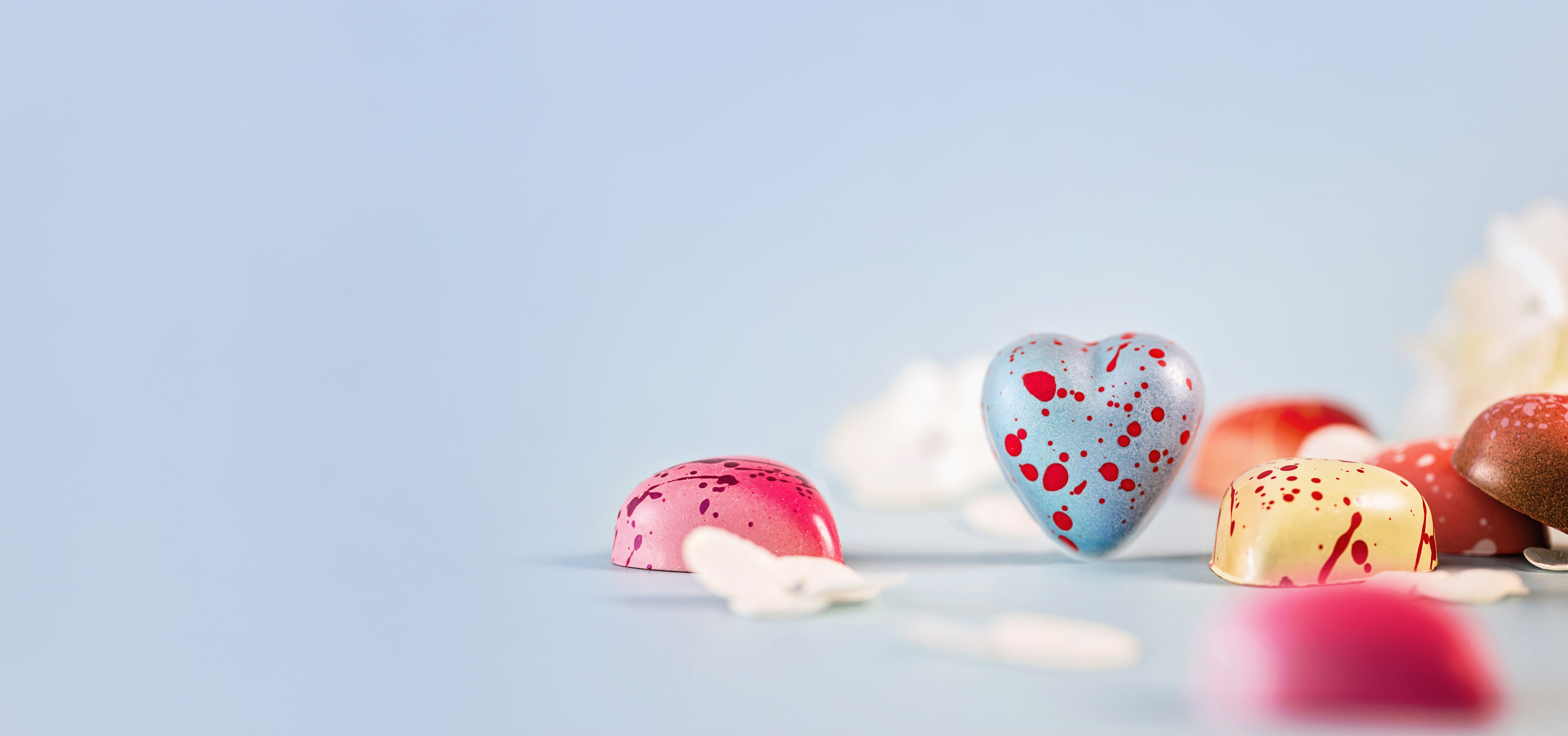 Heart-shaped truffle boxes on pink background. Roses, truffles and champagne glasses surround truffles. 