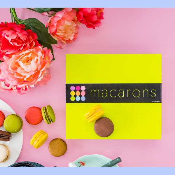 Individual and boxed macaroons on a pink background. Pink flowers in top left corner.